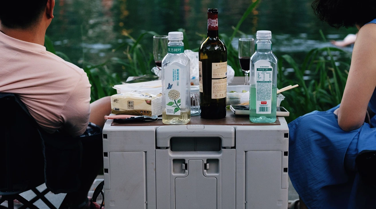Electric portable fridge and traditional ice cooler placed side by side at a campsite
